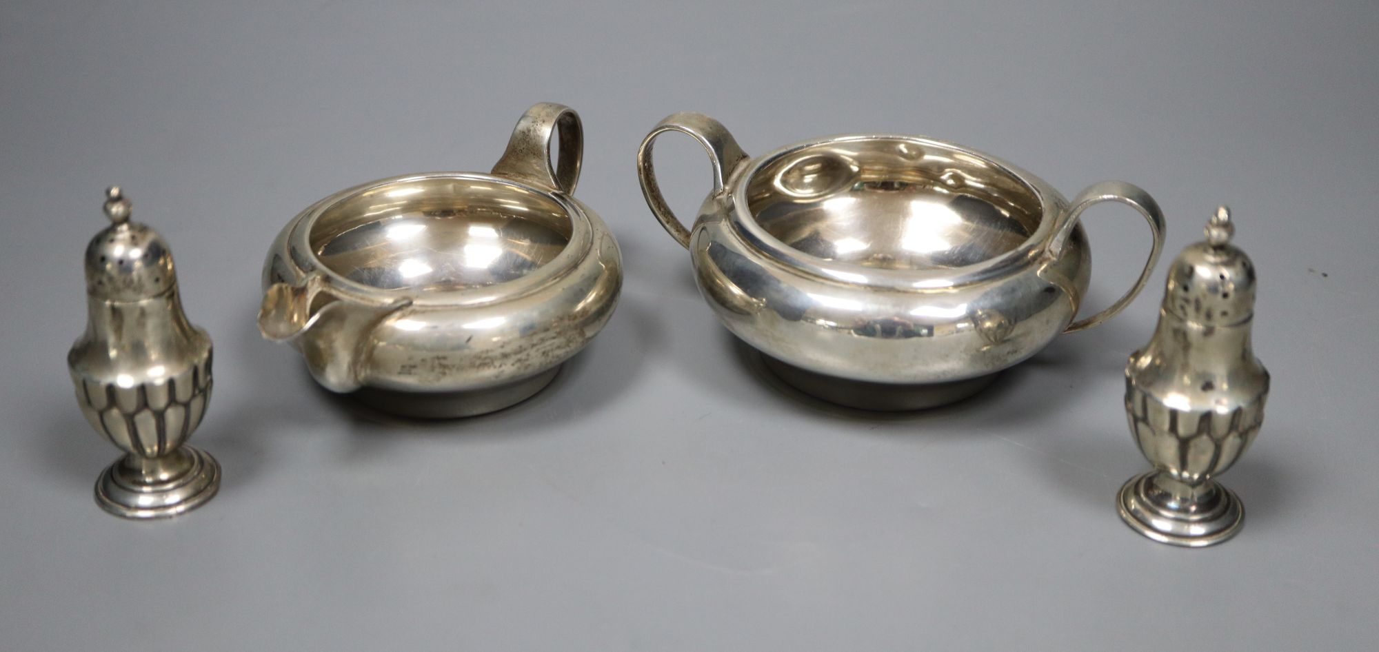 A George V silver sugar bowl and cream jug, London 1935 and a pair of Edwardian silver salt and pepper pots, London 1905,